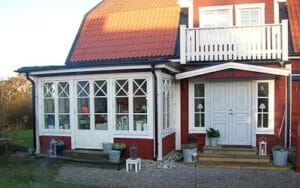 Röd trävilla med vit glasveranda med krysspröjsade fönster och vit entrédörr med balkong ovanför.