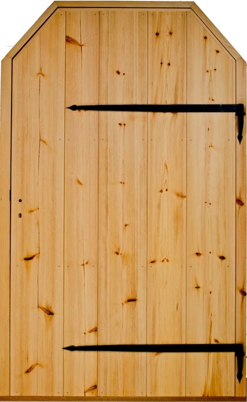 Rustik innerdörr i naturfärgat trä med synliga kvistar, stående brädor och svart smidda gångjärn, samt snedskurna hörn upptill.