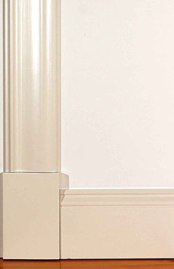 Närbild av vitt fönsterfoder och matchande golvsockel med klassisk profilerad design, monterat mot en slät vit vägg och ett lackat trägolv.