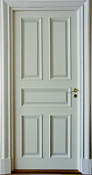 Foto av vit klassisk innerdörr med fem profilerade spegelpaneler och breda, dekorerade dörrfoder runt öppningen.