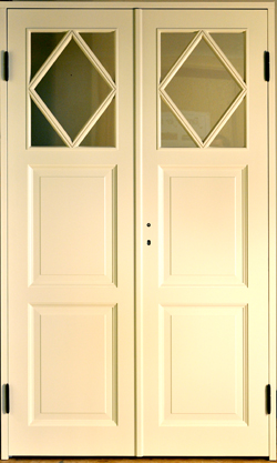 Foto av vit pardörr med en rombformad glasruta i övre delen på varje dörrblad och profilerade spegelpaneler i nedre delarna.