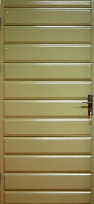 Grön dörr i trä med liggande profilerade panelbrädor. Dörren har en enkel metallhandtag i mörk färg på höger sida och gångjärn på vänster sida.