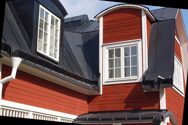 Rött trähus med svart plåttak i brutet takutförande. På övervåningen finns två takkupor med spröjsade vita fönster – en med tvådelat fönster och en med fyrdelat. Taken på kuporna är rundade och belagda med svart plåt. Vita foder ramar in fönstren och kontrasterar mot den röda träpanelen.