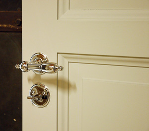 Närbild av vit spegeldörr med klassiskt dörrhandtag i blank metall på rund rosett och matchande runt vredbeslag undertill.