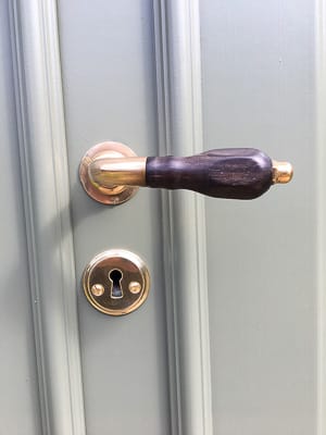 Närbild av dörrhandtag och nyckelhål på målad spegeldörr, med tydliga metallreflexer i ljuset.