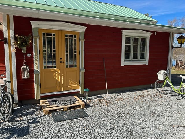 Fasad med gul fönsterdörr med spröjsat glas och intilliggande vitmålat fönster med karmar och foder