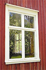 Tvåluftsfönster med vitmålade karmar och mittpost, monterat i en röd träfasad där träd och grönska speglas i glaset.