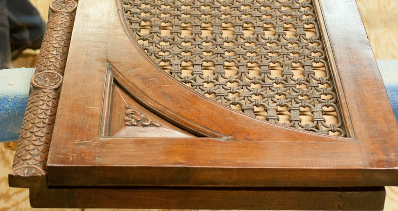 Närbild av en äldre, rikt dekorerad trädörr eller dörrpanel med mörk patina. Träet är snidat med ornamentala detaljer och rundade profiler, och mittfältet består av ett flätat eller genombrutet mönster i trä. Ytan visar spår av ålder och hantverk, vilket ger ett tydligt historiskt och antikt uttryck.